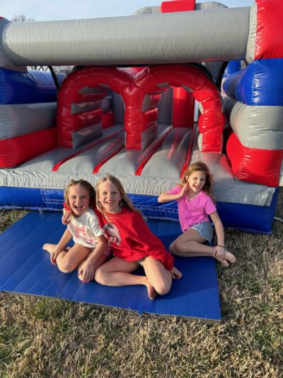 a group of girls sitting on a mat in front of a bouncy castle